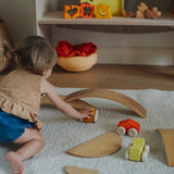 A child playing with the orange Grimm's wooden stacking car toys driving them under a Grimm's bridge piece. These Grimm's toys are part of a wide range of wooden toys available here at Babipur. 