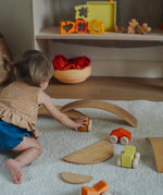 A child playing with the orange Grimm's wooden stacking car toys driving them under a Grimm's bridge piece. These Grimm's toys are part of a wide range of wooden toys available here at Babipur. 