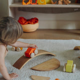 A child playing with the orange Grimm's wooden stacking car toys driving them over a Grimm's bridge piece. These Grimm's toys are part of a wide range of wooden toys available here at Babipur. 