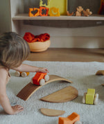A child playing with the orange Grimm's wooden stacking car toys driving them over a Grimm's bridge piece. These Grimm's toys are part of a wide range of wooden toys available here at Babipur. 