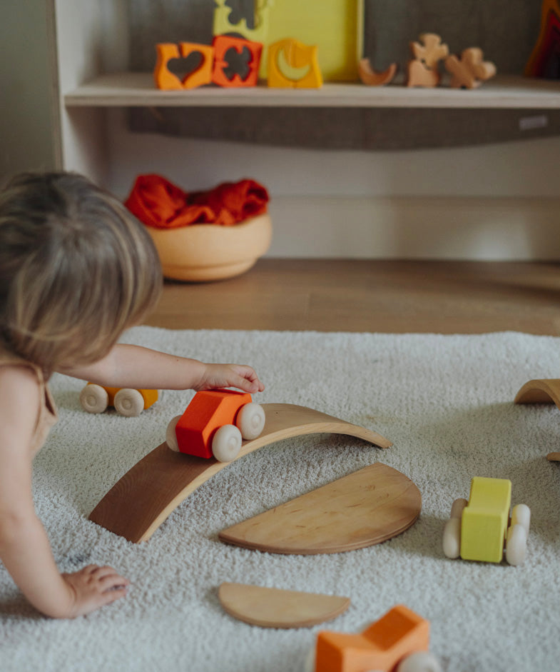 A child playing with the orange Grimm's wooden stacking car toys driving them over a Grimm's bridge piece. These Grimm's toys are part of a wide range of wooden toys available here at Babipur. 
