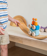 A child playing with the blue Grimm's wooden stacking car toys placing them on a Grimm's bridge piece. These Grimm's toys are part of a wide range of wooden toys available here at Babipur. 
