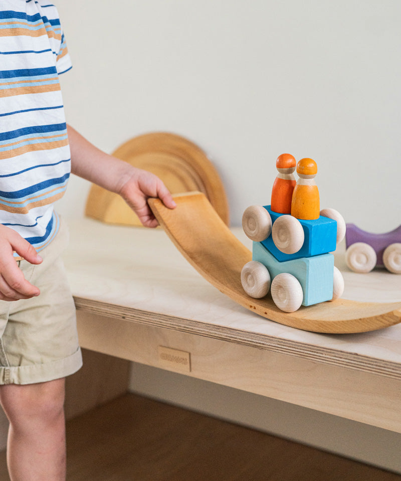 A child playing with the blue Grimm's wooden stacking car toys placing them on a Grimm's bridge piece. These Grimm's toys are part of a wide range of wooden toys available here at Babipur. 