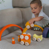 A child playing with the yellow Grimm's wooden stacking car toys driving them over a Grimm's rainbow piece. These Grimm's toys are part of a wide range of wooden toys available here at Babipur. 