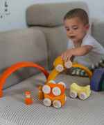 A child playing with the yellow Grimm's wooden stacking car toys driving them over a Grimm's rainbow piece. These Grimm's toys are part of a wide range of wooden toys available here at Babipur. 