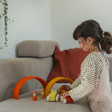 A child playing with the orange Grimm's wooden stacking car toys driving them under Grimm's rainbow arches. These Grimm's toys are part of a wide range of wooden toys available here at Babipur. 