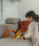A child playing with the orange Grimm's wooden stacking car toys driving them under Grimm's rainbow arches. These Grimm's toys are part of a wide range of wooden toys available here at Babipur. 