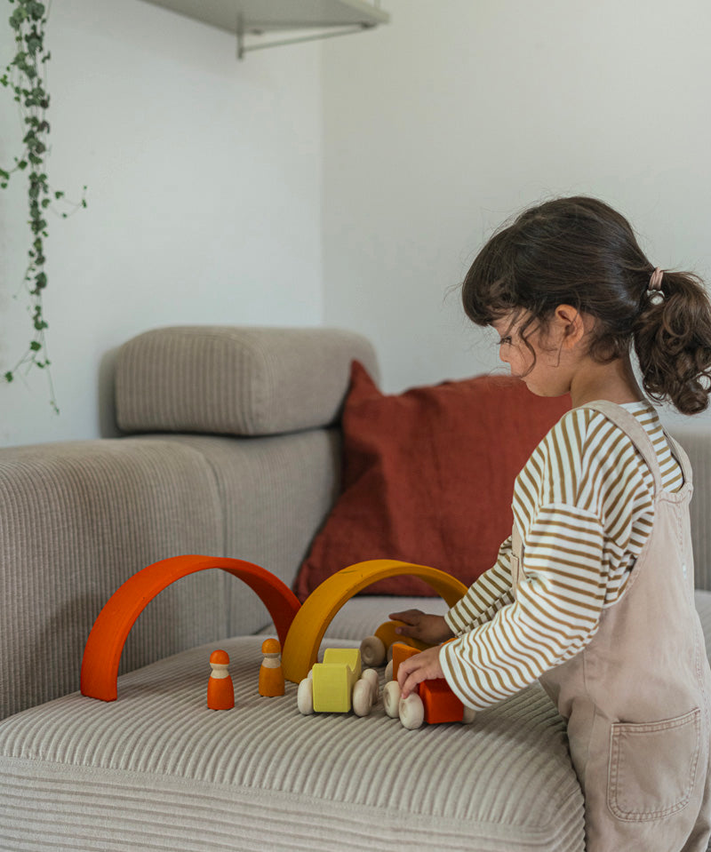 A child playing with the orange Grimm's wooden stacking car toys driving them under Grimm's rainbow arches. These Grimm's toys are part of a wide range of wooden toys available here at Babipur. 