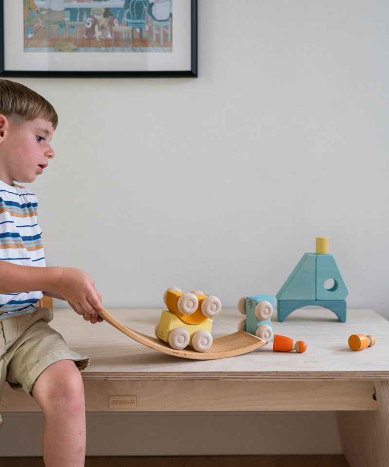 A child playing with the yellow Grimm's wooden stacking car toys placing them on a Grimm's bridge piece. These Grimm's toys are part of a wide range of wooden toys available here at Babipur. 