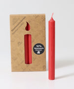 A pack of 12 Red 10% beeswax candles by Grimm's with one red candles placed in front of the box.
