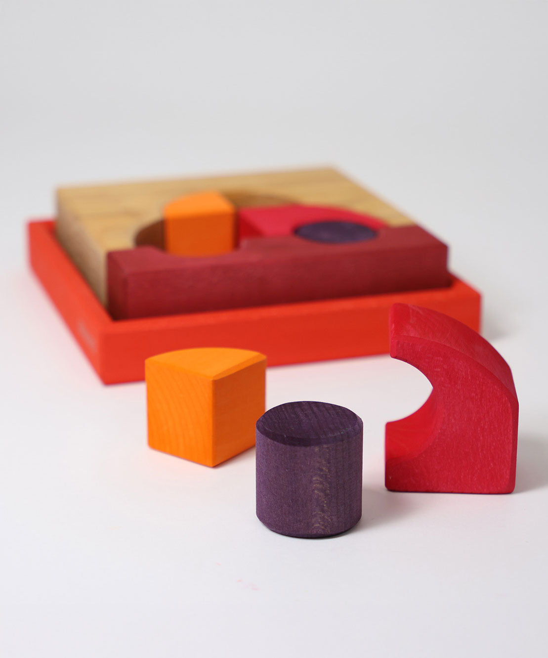 Three blocks from the Grimm's red building set taken out of the wooden tray that they come in. The tray and the rest of the blocks can be seen in the background. These Grimm's toys are part of a wide range of wooden toys available here at Babipur. 