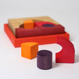Three blocks from the Grimm's red building set taken out of the wooden tray that they come in. The tray and the rest of the blocks can be seen in the background. These Grimm's toys are part of a wide range of wooden toys available here at Babipur. 