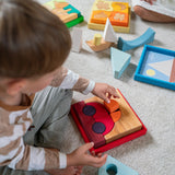 An overhead view of the a child playing with the Grimm's red car stacking puzzle building block set. These Grimm's toys are part of a wide range of wooden toys available here at Babipur. 