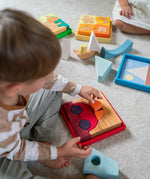 An overhead view of the a child playing with the Grimm's red car stacking puzzle building block set. These Grimm's toys are part of a wide range of wooden toys available here at Babipur. 