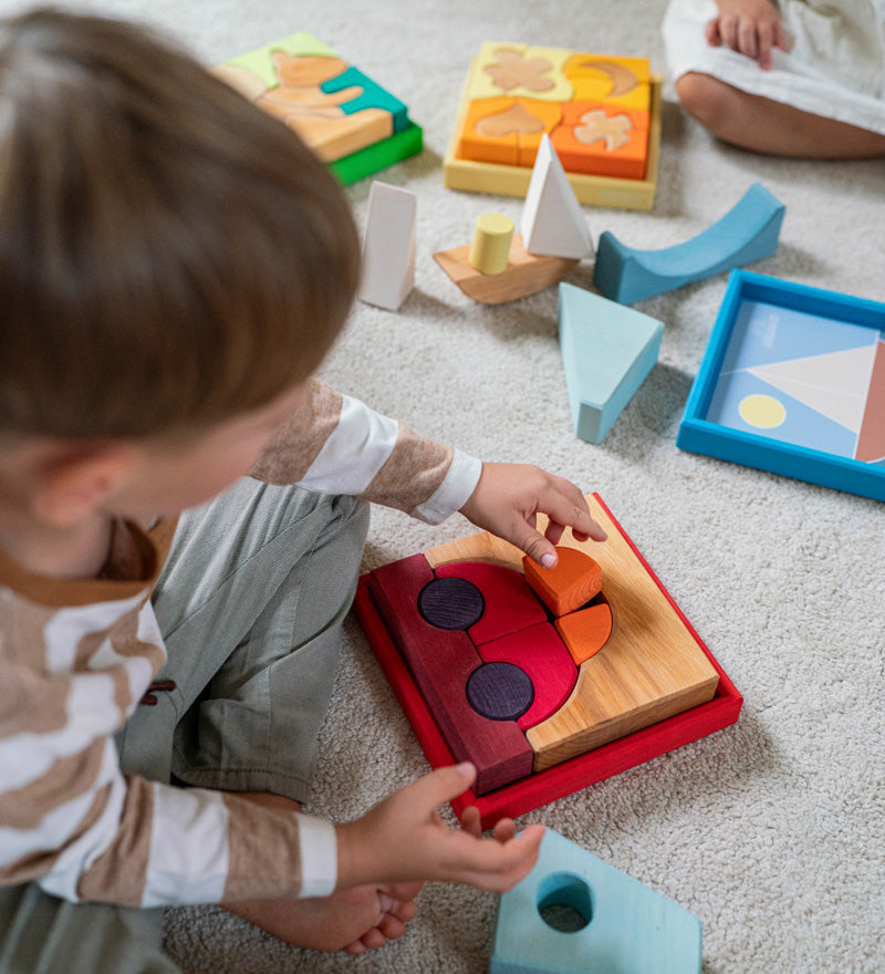 An overhead view of the a child playing with the Grimm's red car stacking puzzle building block set. These Grimm's toys are part of a wide range of wooden toys available here at Babipur. 
