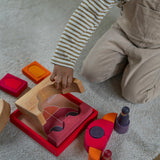 An overhead view of the a child playing with the Grimm's red car stacking puzzle building block set. These Grimm's toys are part of a wide range of wooden toys available here at Babipur. 
