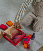 An overhead view of the a child playing with the Grimm's red car stacking puzzle building block set. These Grimm's toys are part of a wide range of wooden toys available here at Babipur. 