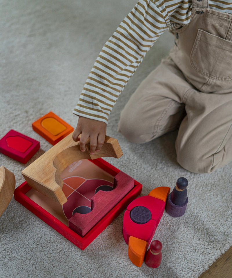 An overhead view of the a child playing with the Grimm's red car stacking puzzle building block set. These Grimm's toys are part of a wide range of wooden toys available here at Babipur. 