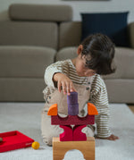 A child playing with the Grimm's red car stacking puzzle building block set stacking the pieces on top of each other. These Grimm's toys are part of a wide range of wooden toys available here at Babipur. 