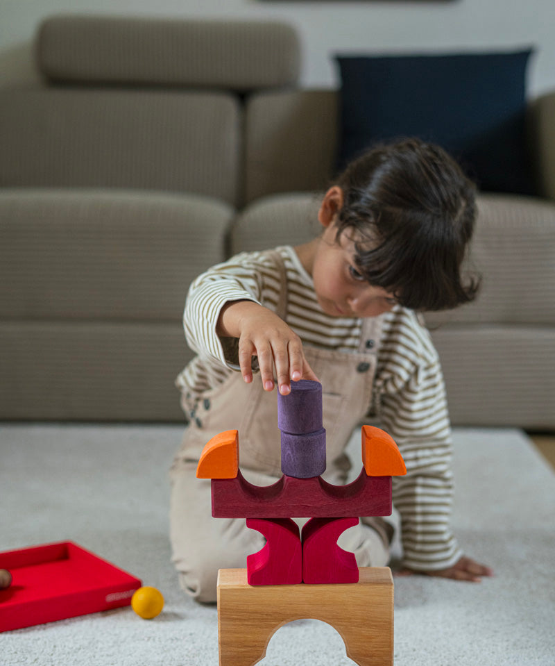 A child playing with the Grimm's red car stacking puzzle building block set stacking the pieces on top of each other. These Grimm's toys are part of a wide range of wooden toys available here at Babipur. 