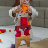 A child playing with the Grimm's red car stacking puzzle building block set stacking pieces from the Grimm's window set on top of a stack of the blocks. These Grimm's toys are part of a wide range of wooden toys available here at Babipur. 