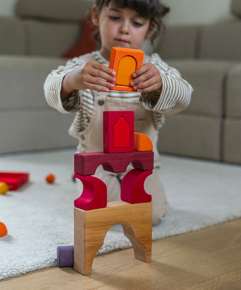 A child playing with the Grimm's red car stacking puzzle building block set stacking pieces from the Grimm's window set on top of a stack of the blocks. These Grimm's toys are part of a wide range of wooden toys available here at Babipur. 