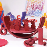 Grimms red wooden figures from the counting and story telling set standing on a red which is sitting inside a red rainbow arch. This set is available at Babipur.