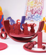 Grimms red wooden figures from the counting and story telling set standing on a red which is sitting inside a red rainbow arch. This set is available at Babipur.