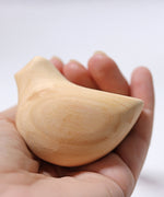 A close up of the Grimm's wooden relaxing bird toy in the placed in the palm of an adult's hand.