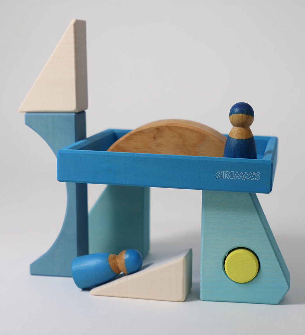 The blocks from the Grimm's Building Set Blue used in a small world play scene with two Grimm's friends wooden peg dolls. These Grimm's wooden block sets are part of a wide range of wooden toys available here at Babipur.