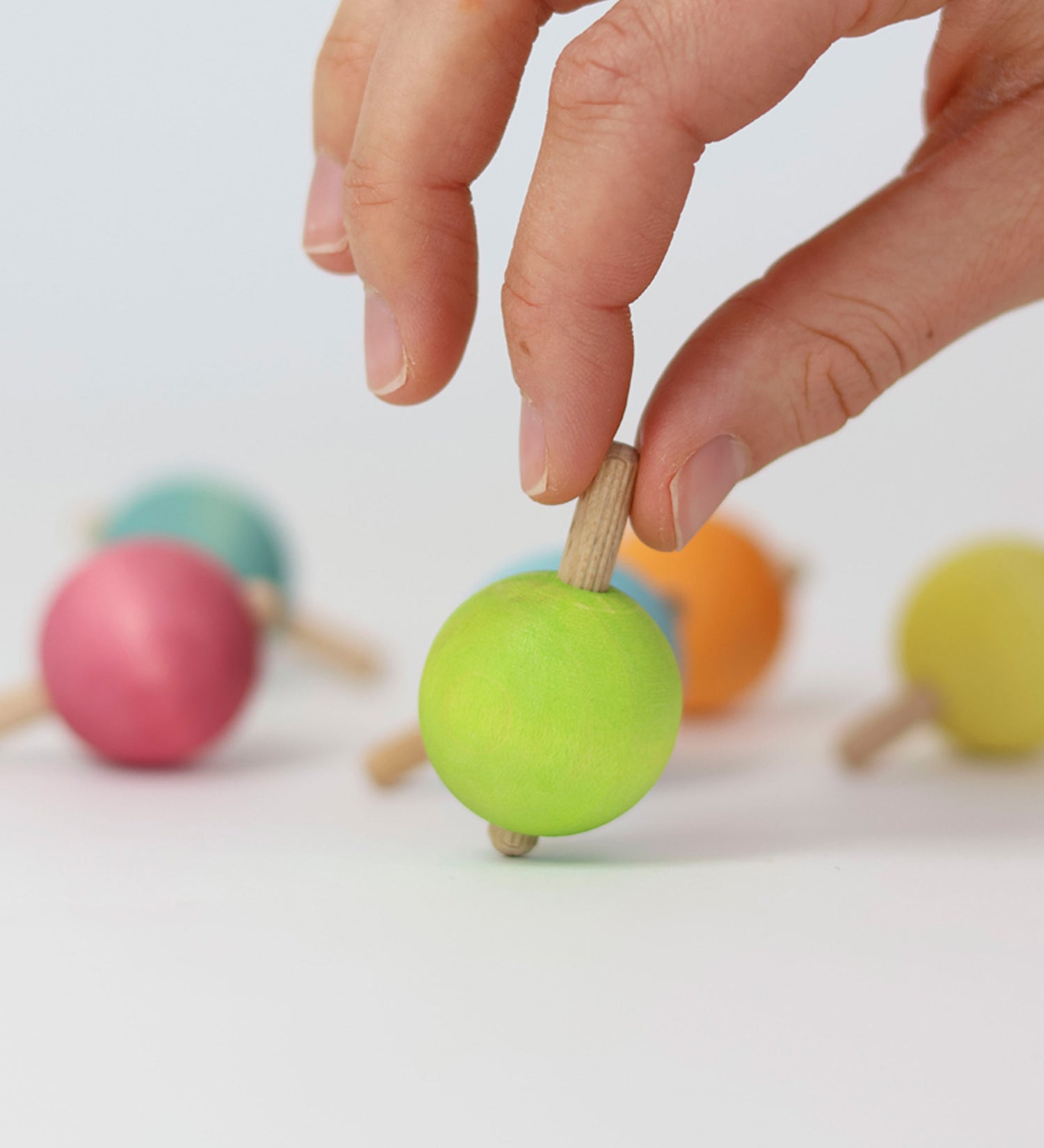 A hand ready to spin the green pastel wooden spinning top from Grimm's. 