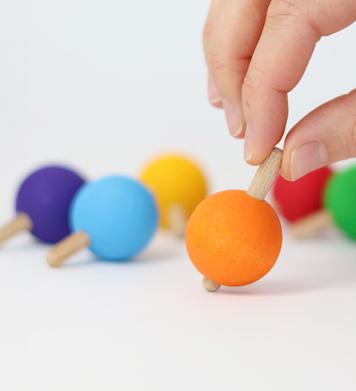 A hand ready to spin the orange wooden spinning top from Grimm's. 