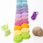 The buttons from the Grimm's buttons threading game lined up on a flat surface with the thread and a snail shell next to them. 