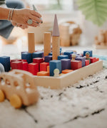 Adult stacking different building blocks on a Grimms small counting block in Grimm’s World of Numbers palette 