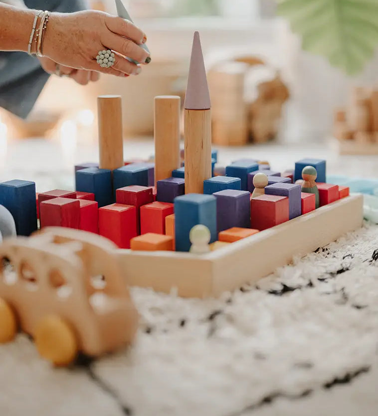 Adult stacking different building blocks on a Grimms small counting block in Grimm’s World of Numbers palette 