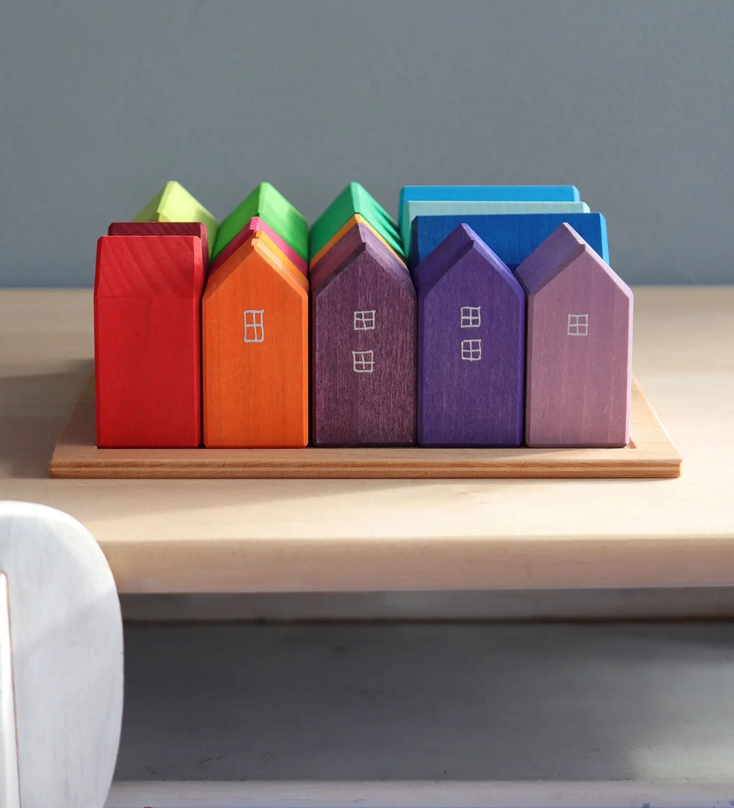 Grimm's small rainbow wooden houses set. 15 different colour houses in various sizes on a wooden plinth tray.