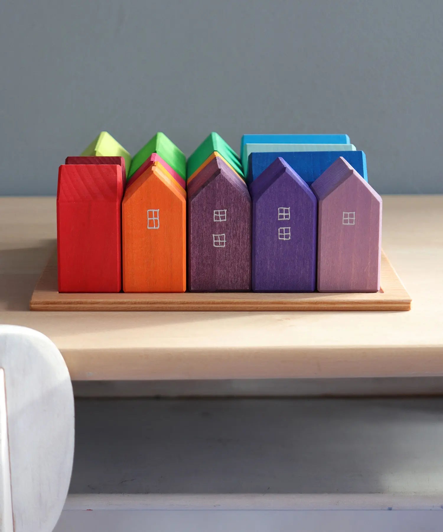 Grimm's small rainbow wooden houses set. 15 different colour houses in various sizes on a wooden plinth tray.