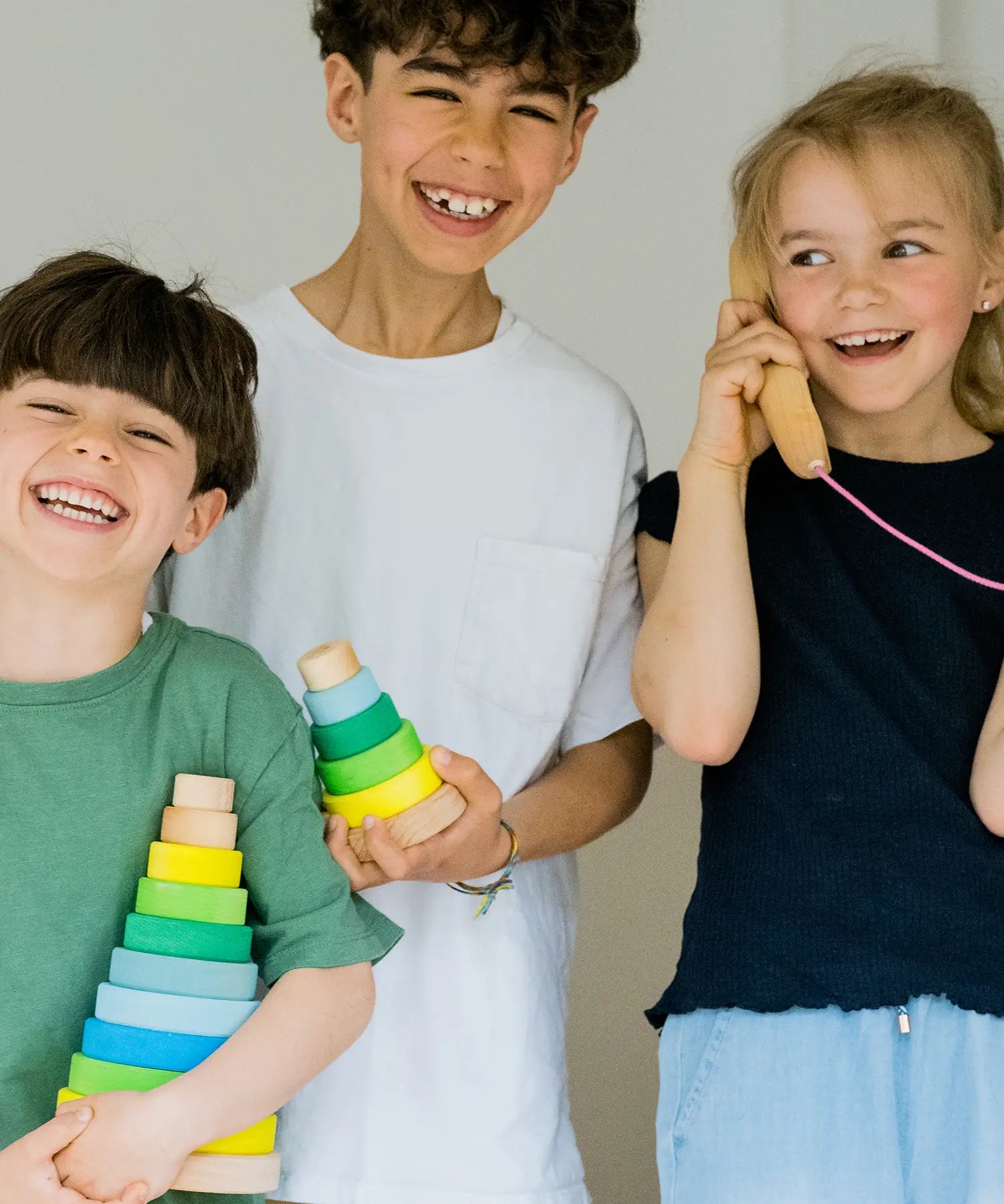 Children holding a small and large Grimms neon green conical stacking towers