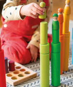 Child playing with the Grimm's large and small building rollers in a rainbow palette stacking friends peg dolls on top. 