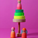 A tree made from loose wooden neon green Grimms conical tower pieces with a peg doll on top