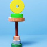 Loose small Grimms neon green conical pieces stacked under the natural base and peg with a conical piece balancing on top