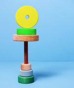 Loose small Grimms neon green conical pieces stacked under the natural base and peg with a conical piece balancing on top