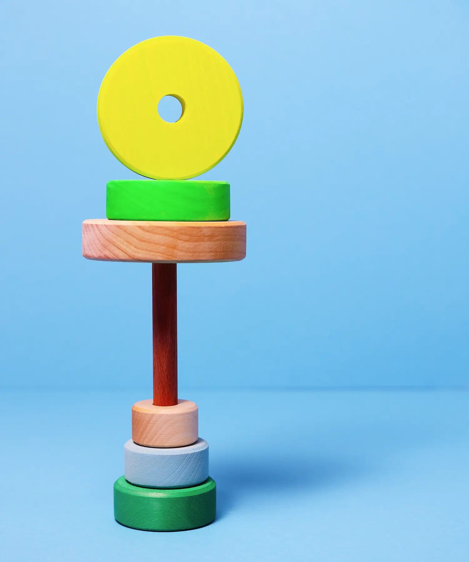 Loose small Grimms neon green conical pieces stacked under the natural base and peg with a conical piece balancing on top
