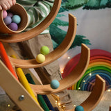 A child tipping out a tub of Grimm's small pastel balls onto a ball run created using the Grimm's natural rainbow and a Triclmb climbing frame.
These Grimm's toys are part of a wide range of wooden toys available here at Babipur.  