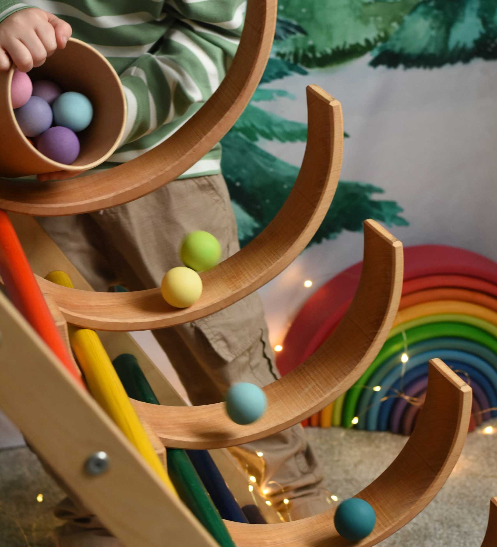 A child tipping out a tub of Grimm's small pastel balls onto a ball run created using the Grimm's natural rainbow and a Triclmb climbing frame.
These Grimm's toys are part of a wide range of wooden toys available here at Babipur.  