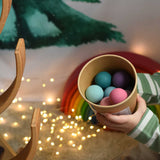 A child holding a tub full of Grimm's small pastel wooden balls. These Grimm's toys are part of a wide range of wooden toys available here at Babipur. 