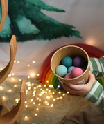 A child holding a tub full of Grimm's small pastel wooden balls. These Grimm's toys are part of a wide range of wooden toys available here at Babipur. 