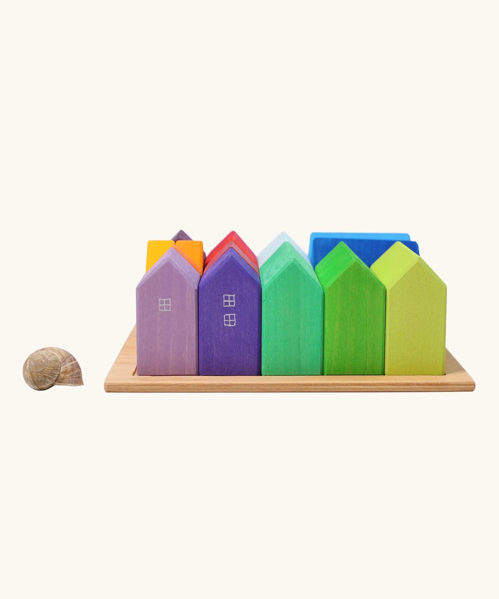 Grimm's small rainbow wooden houses set placed next to a snail's shell. 15 different colour houses in various sizes.