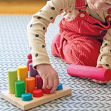 Child sorting individual Grimms small wooden stacking rollers in its sorting tray and holding a large roller showing scale