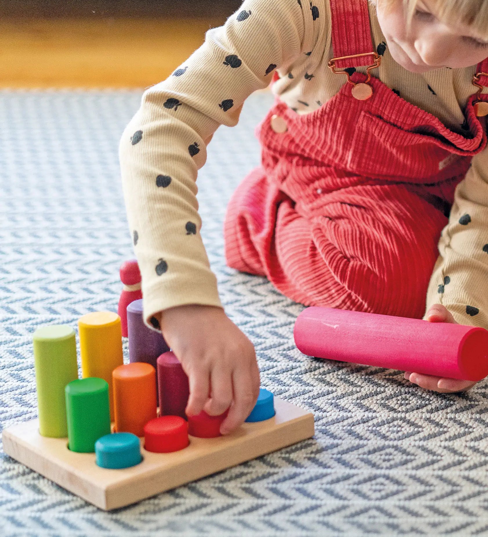 Child sorting individual Grimms small wooden stacking rollers in its sorting tray and holding a large roller showing scale